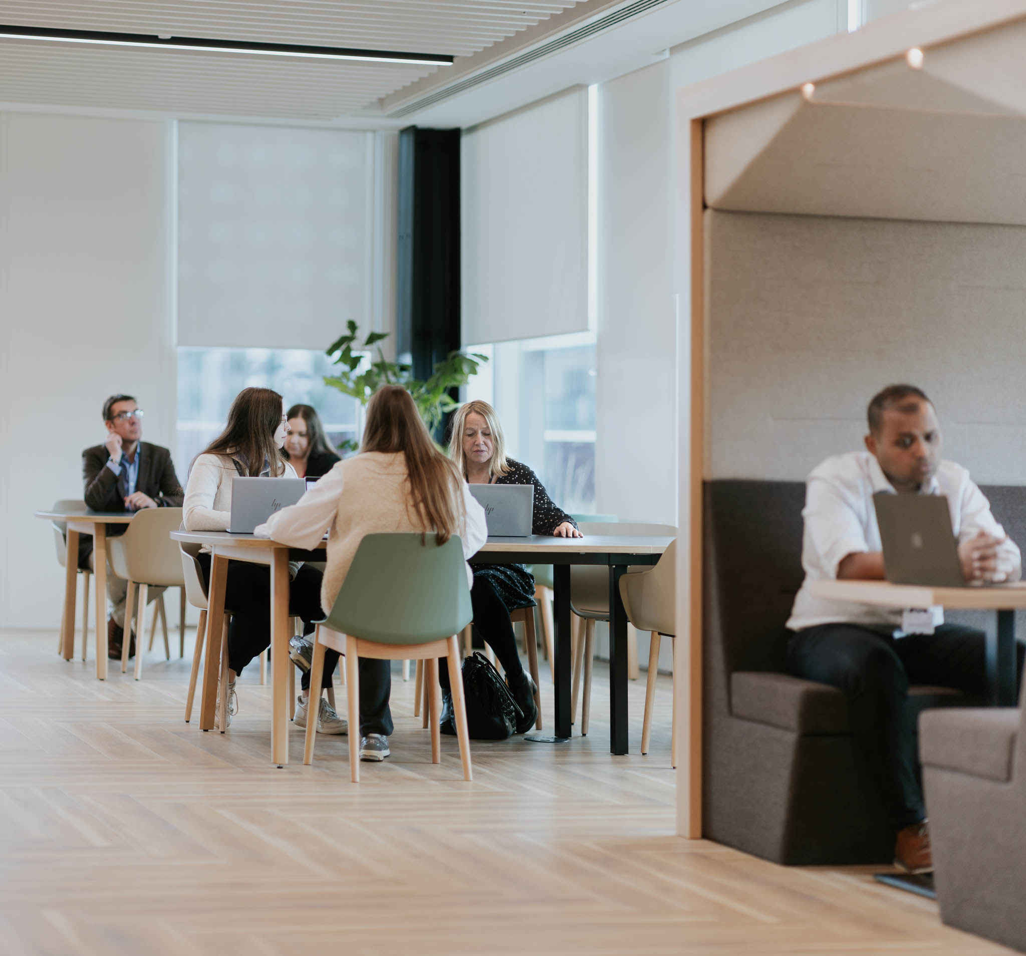 Civil servants working in a collaboration zone. In the foreground, an individual is working in an enclosed seating booth to reduce sounds and distractions.