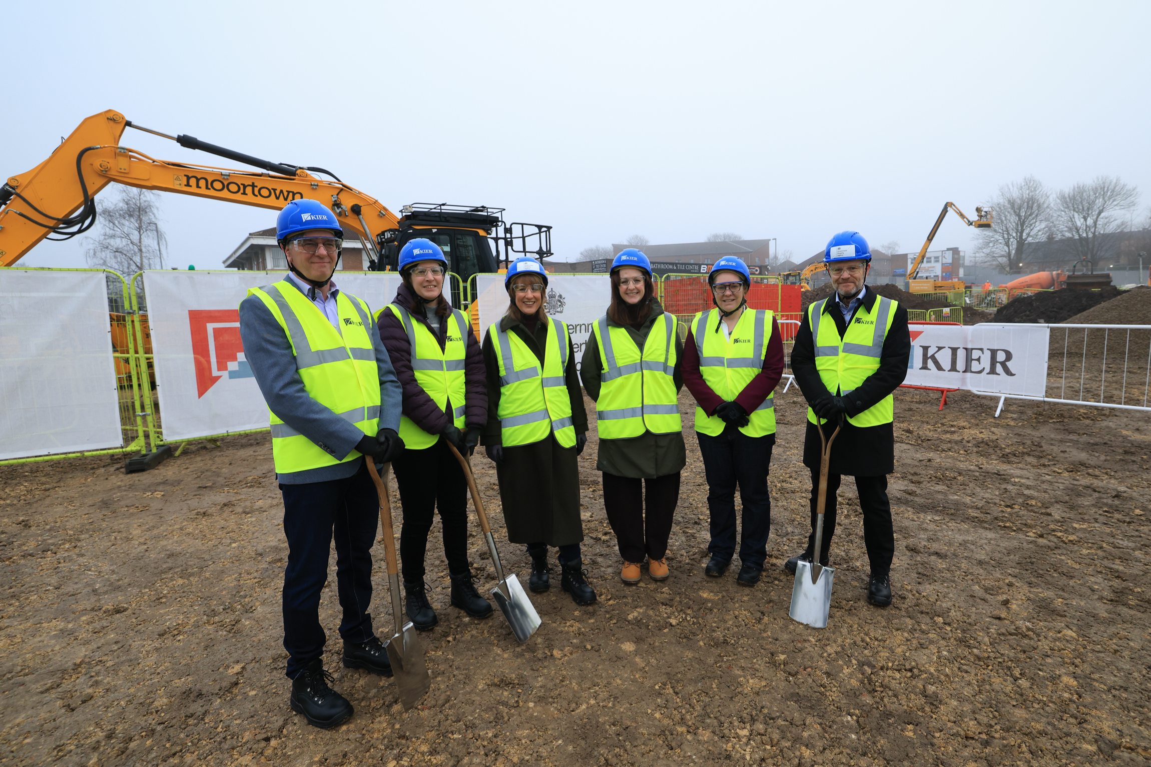 Six people, including UK Chancellor Rachel Reeves, standing in a line at a construction site for a groundbreaking ceremony.